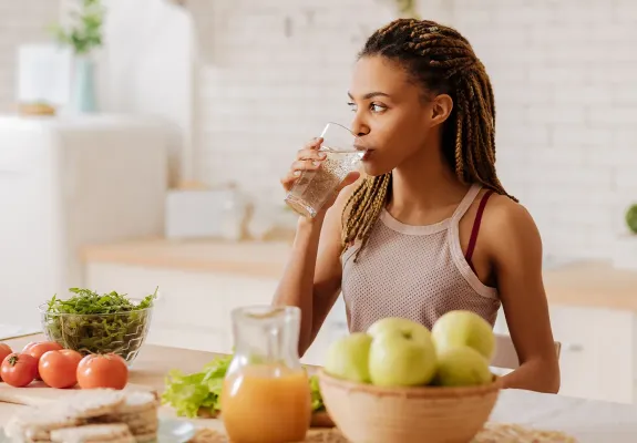 Woman standing at a kitchen countertop drinking a glass of water.